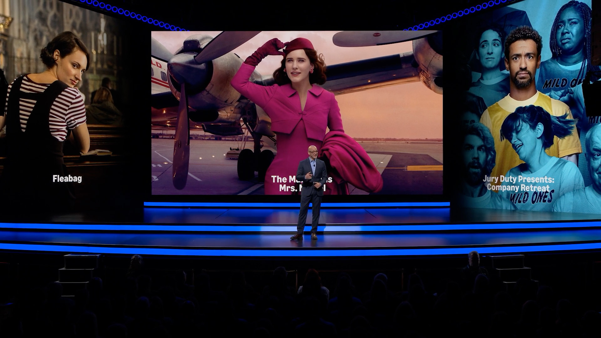 A presenter stands beneath oversized Fleabag, The Marvelous Mrs. Maisel, and The Boys artwork.